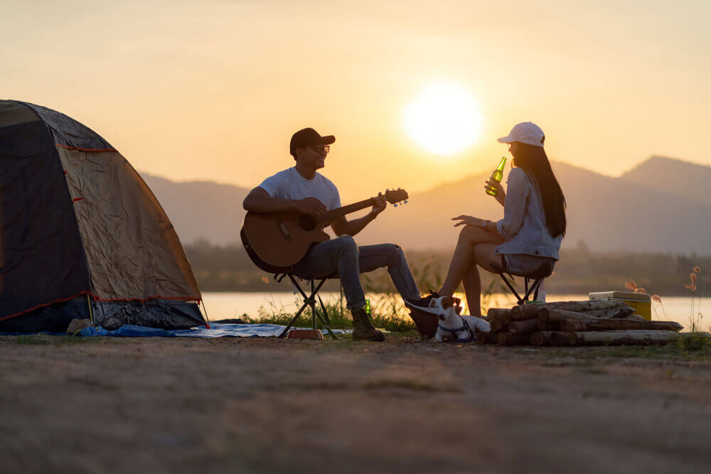 lelaki bermain gitar dan wanita sedang minum semasa berkhemah
