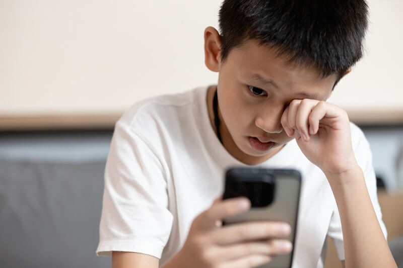 Budak lelaki menggaru mata akibat penggunaan telefon
